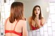 A woman in a red bra and panties brushing her teeth in front of a mirror.