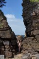 A naked woman standing in the middle of a rocky area.