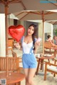 A woman holding a red heart shaped balloon on a beach.