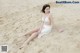 A woman in a white bikini sitting on the sand.