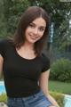 A woman in a black shirt and jeans posing by a pool.