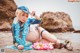 A woman in a bikini and hat sitting on the beach.