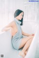 A woman sitting in a bathtub wearing a blue dress.