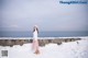 A woman standing in the snow near the ocean.