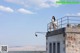 A woman sitting on top of a building on a balcony.