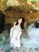 A woman in a white dress standing in front of a rock.